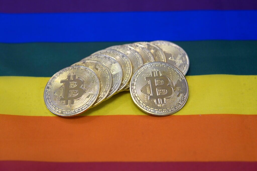 A rainbow flag with a stack of money coins. In this case, these are Bitcoins on the rainbow flag.