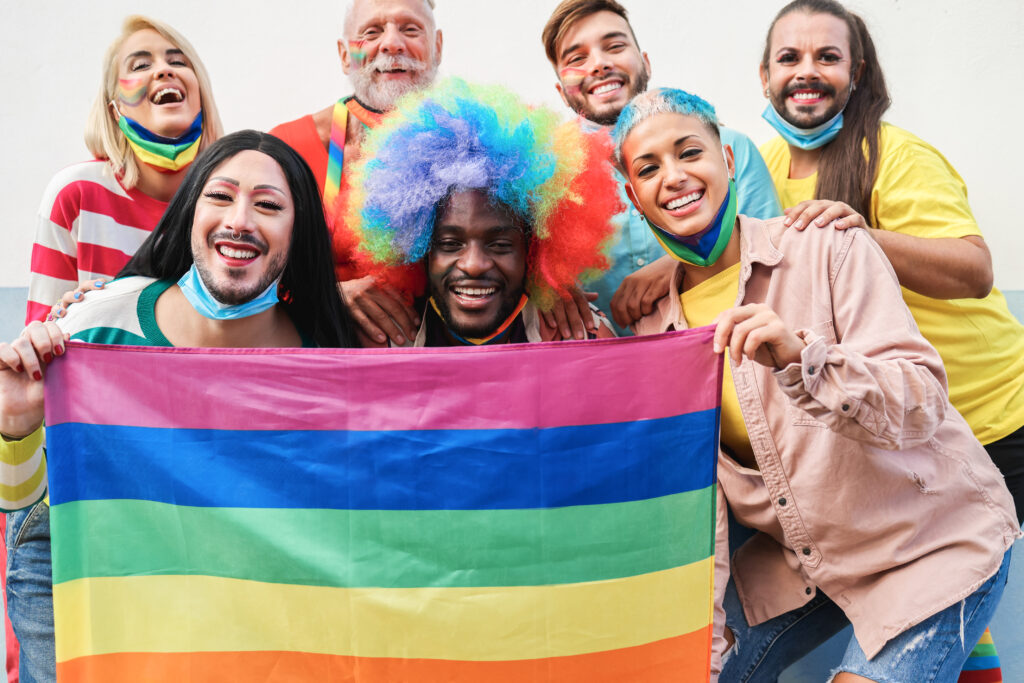 A group of people holding a rainbow flag and smiling to show their diversity as members of the LGBTIQ+ community.