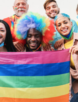 A group of people holding a rainbow flag and smiling to show their diversity as members of the LGBTIQ+ community.